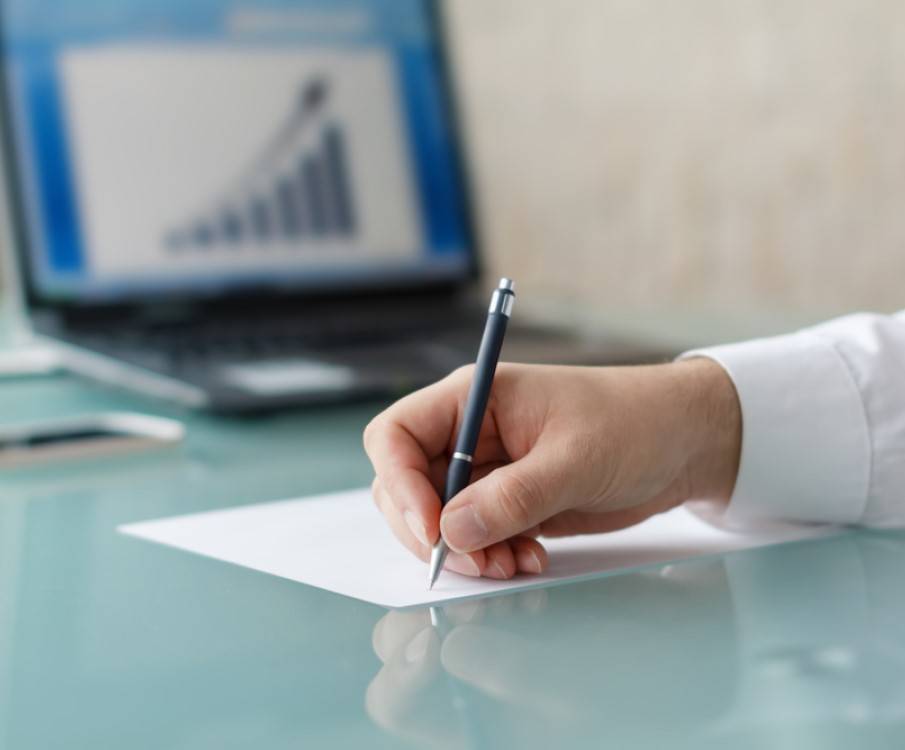 hand schrijft op papier en laptop met grafiek op achtergrond