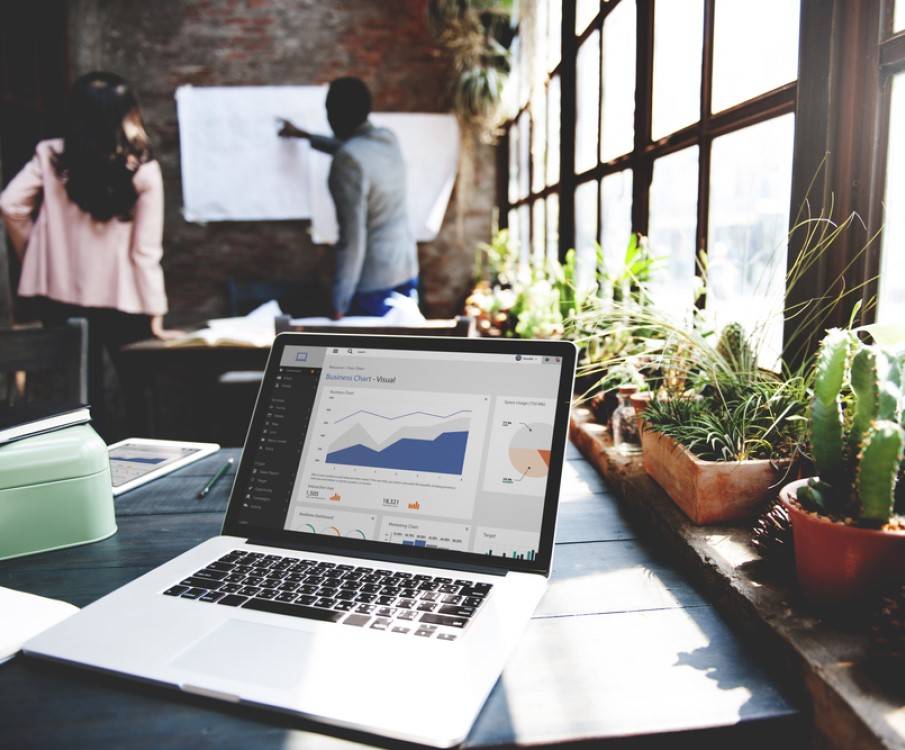 man en vrouw overleggen op achtergrond en er staat een laptop op tafel met planten in het venster